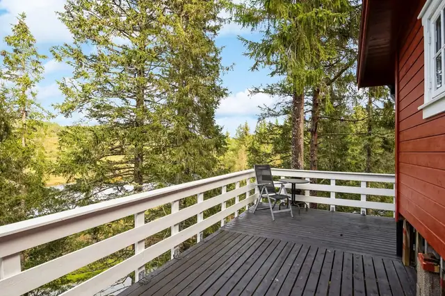 En romslig terrasse med hvitt rekkverk og utsikt over frodig skogsterreng. Perfekt for avslapning med god plass til sittegrupper.