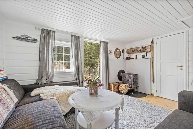 Hjemmekoselig atmosfære med peisovn, myke tekstiler og store vinduer som slipper inn naturlig lys fra de naturskjønne omgivelsene.