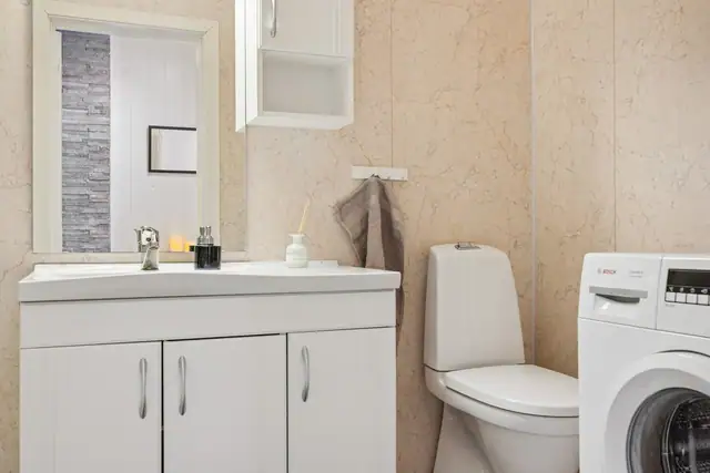 Badet er utstyrt med toalett, servant i innredning, dusjkabinett og opplegg for vaskemaskin.