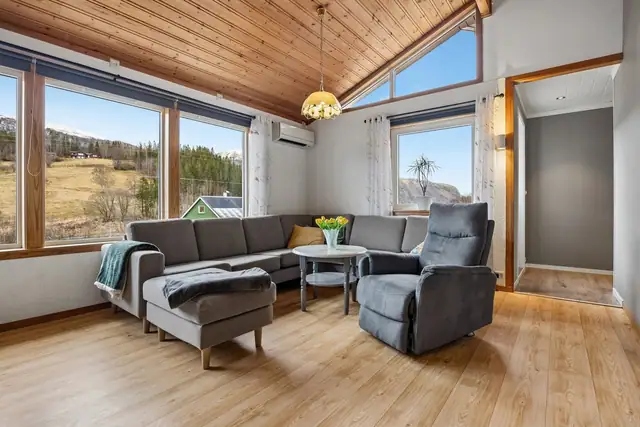 Stuen er romslig med en lun og innbydende atmosfære, preget av gjennomgående treverk i himlingen som gir karakter og varme.