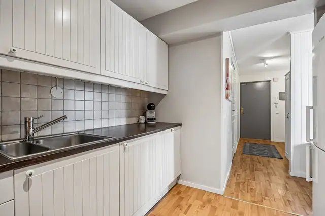 Tidløst kjøkken med hvite fronter, integrerte hvitevarer som oppvaskmaskin, komfyr og koketopp.