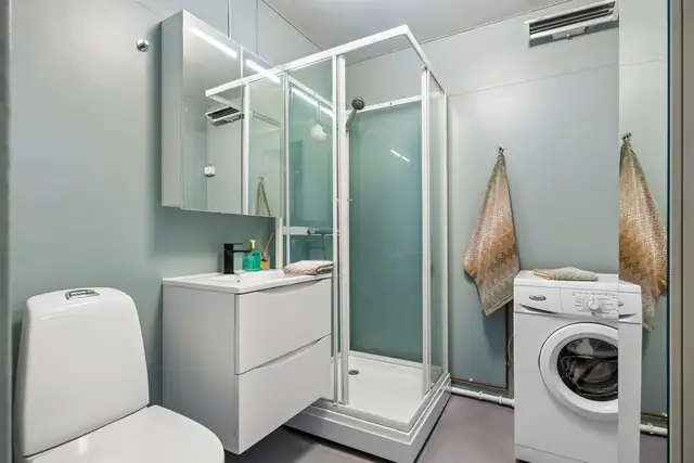 Badet er innredet med dusjkabinett, servantinnredning og opplegg for vaskemaskin.