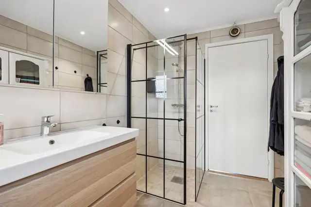 Badet er flislagt på både gulv og vegg, og fremstår med en moderne løsning med vegghengt klosett og romslig dusjhjørne - et stilrent og funksjonelt rom.